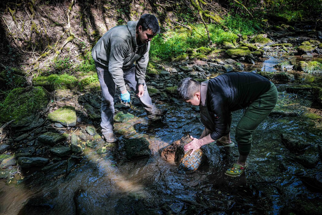 Two volunteers lift a rusted barrel from the Spangerbach creek during the annual creek cleanup in Spangdahlem, Germany, April 25, 2026. The 52nd Civil Engineer Squadron's environmental office coordinates the base's participation in the annual event to demonstrate the importance of protecting shared waterways affected by installation operations. (U.S. Air Force photo by Master Sgt. Alexander W. Riedel)