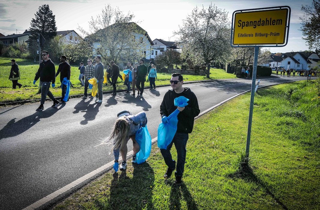 Volunteers walk past the Spangdahlem road sign as they head toward the Spangerbach creek during the annual creek cleanup in Spangdahlem, Germany, April 25, 2026. Groups split up by age and ability before fanning out through the surrounding landscape to collect debris and trash from the waterway and its banks. (U.S. Air Force photo by Master Sgt. Alexander W. Riedel)