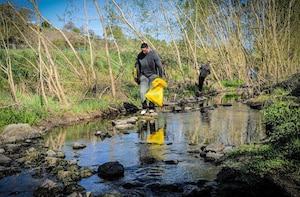Senior Airman Albert Morel, at front, and Tech. Sgt. Benjamin Sisson, both assigned to 52nd Fighter Wing Staff Agencies, search for debris in the Spangerbach creekbed during the annual creek cleanup in Spangdahlem, Germany, April 25, 2026. Volunteers climbed into the creek's ravines and streambed to remove trash and discarded materials from the waterway. (U.S. Air Force photo by Master Sgt. Alexander W. Riedel)