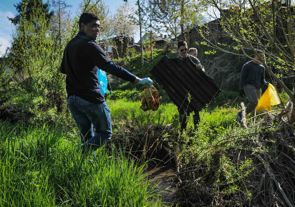 Volunteers remove a corrugated iron roof panel and a plastic bag from the Spangerbach creek during the annual creek cleanup in Spangdahlem, Germany, April 25, 2026. Among the debris collected were old metal drums, building materials, bottles and other discarded items. (U.S. Air Force photo by Master Sgt. Alexander W. Riedel)
