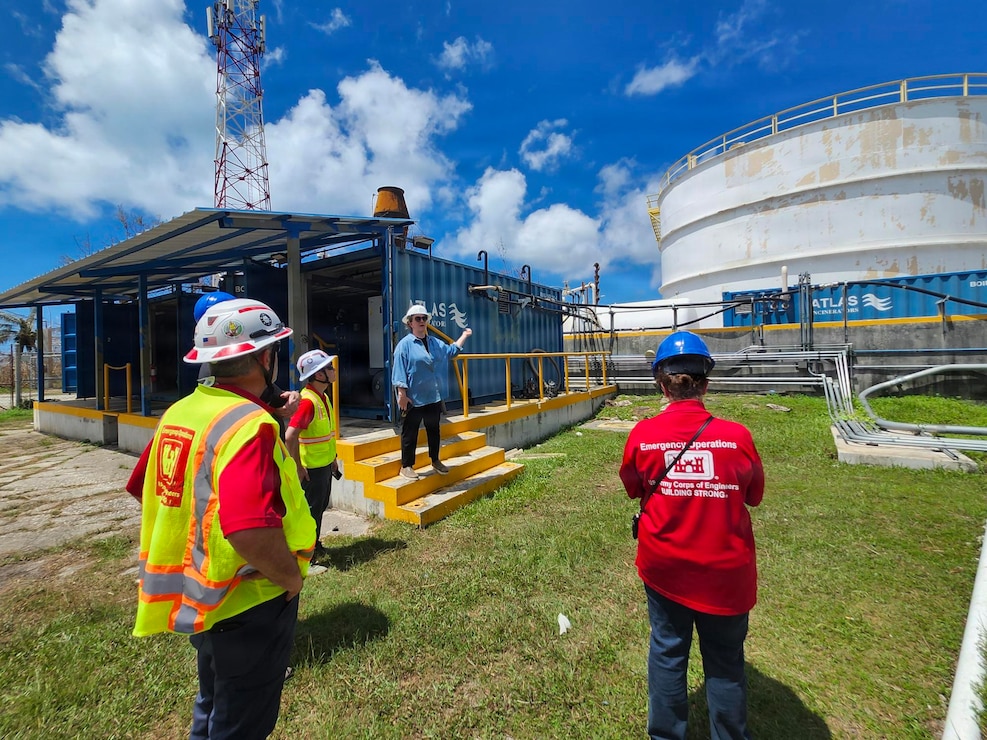 A person is talking to three other people as they come down a small set of stairs at a large fuel depot.