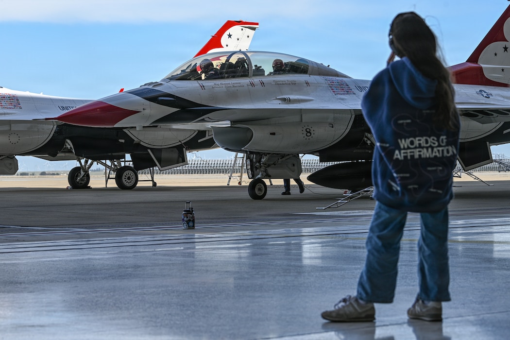 A Little girl stands off to the side looking out at a Thunderbird Demo Team jet