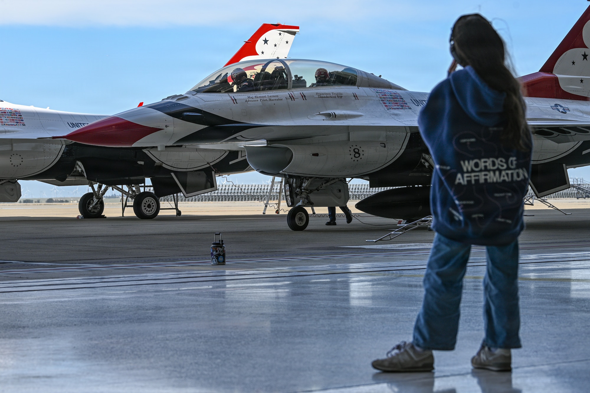 A Little girl stands off to the side looking out at a Thunderbird Demo Team jet