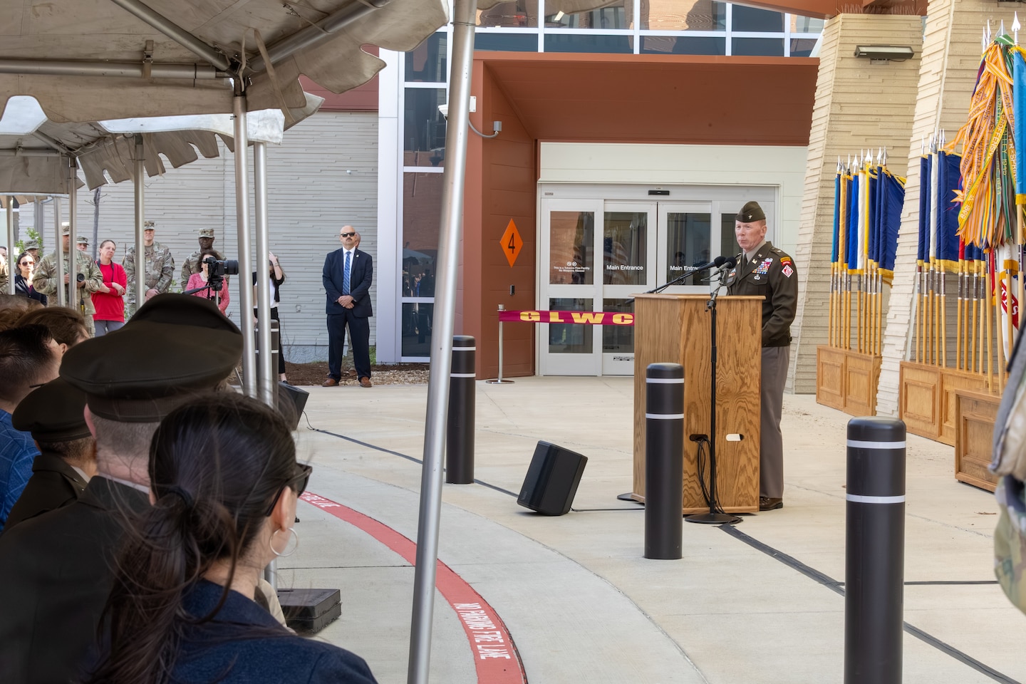 An image of a person speaking at a stand. Behind him, is a ribbon in front of a hospital.