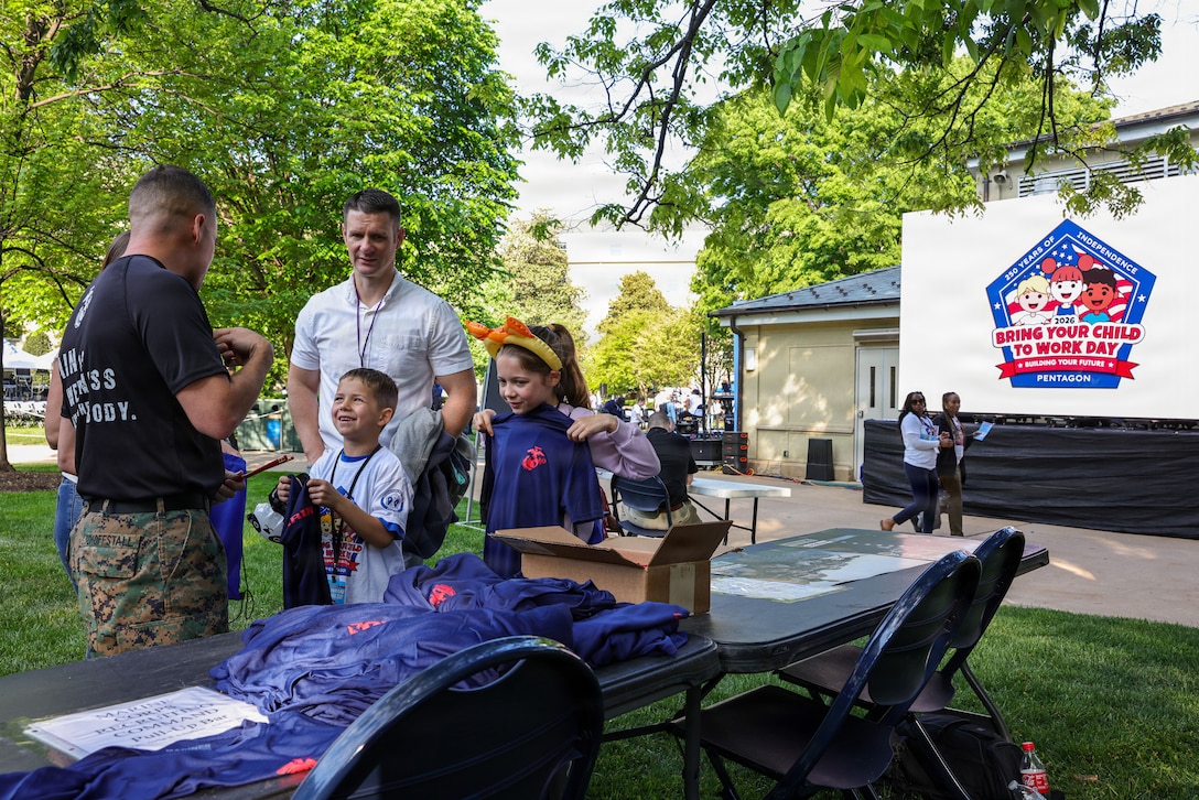 U.S. Marine Corps Master Sgt. Benjamin Schoffstall, a musician technical assistant liaison assigned to Marine Corps Recruiting Command, left, speaks with attendees at the annual Bring Your Child to Work Day event at the Pentagon in Arlington, Va., April 23, 2026. The event allowed the children of Pentagon employees to spend the day with their parents and enjoy attractions from the various branches of service and local high schools. (U.S. Marine Corps photo by Sgt. Aidan Hekker)
