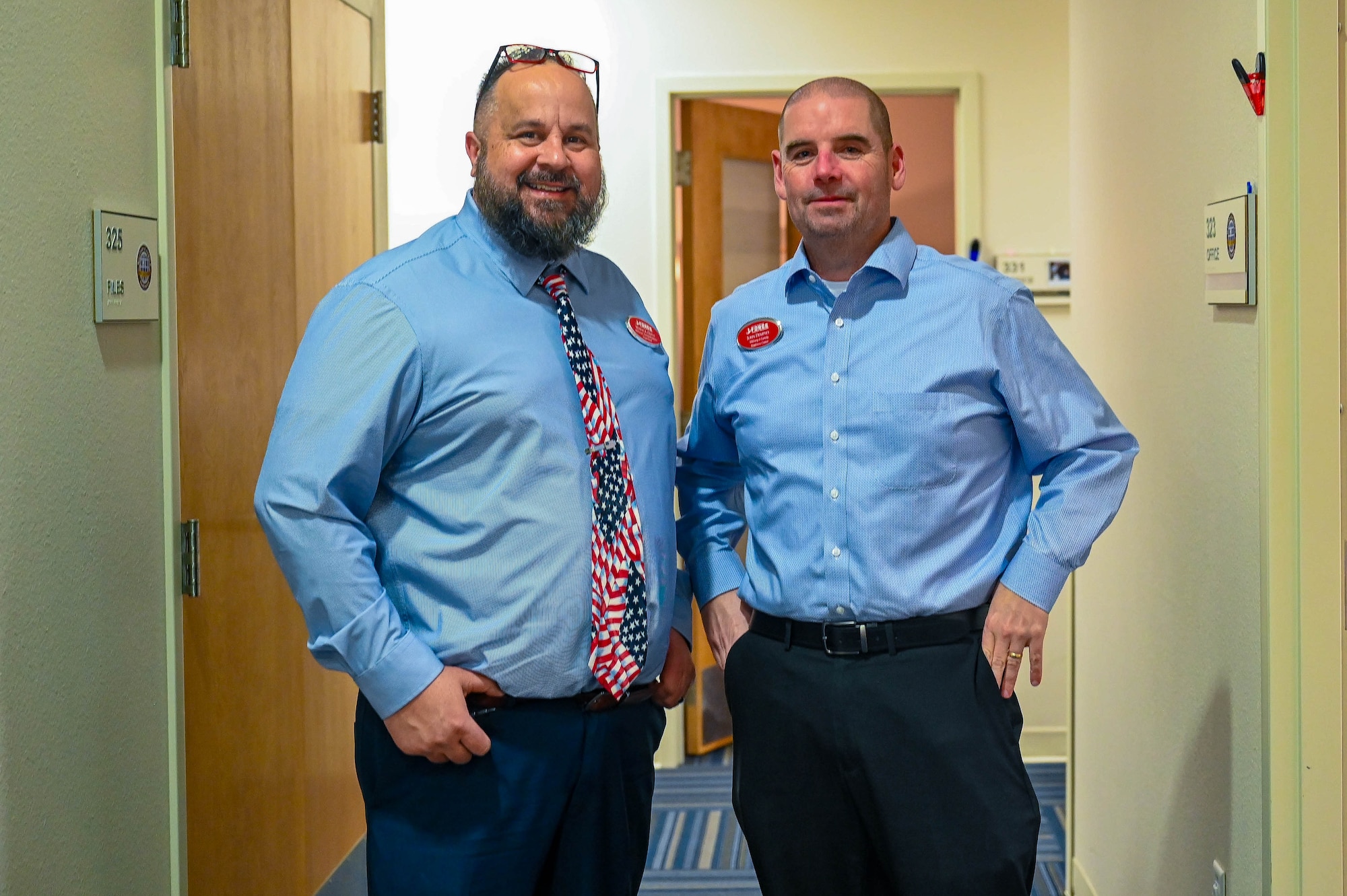 Two men pose for a picture together in a hallway.
