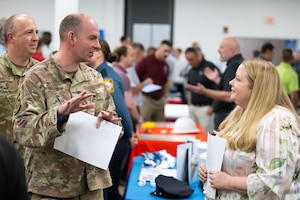 On the left, a man in uniform gestures as he talks with a woman in civilian clothes on the right.