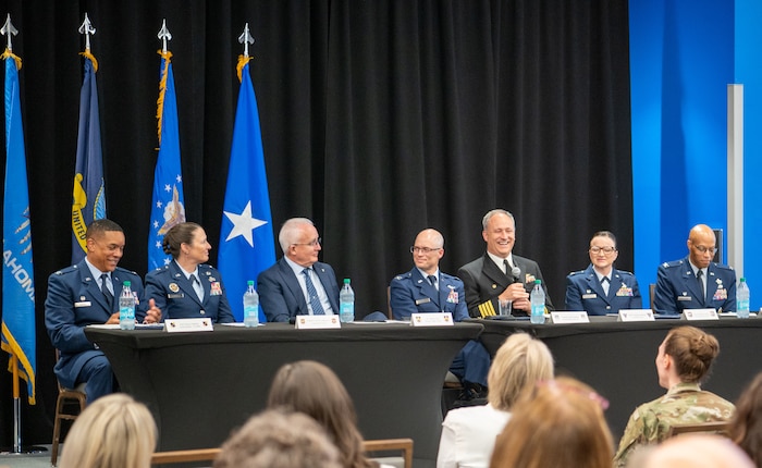 Military members sitting on panel with audience looking on.