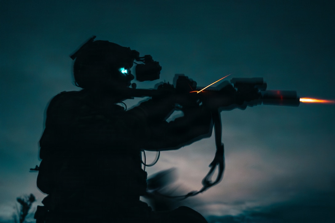 A soldier shown in profile fires a weapon at night. The sky in the background looks teal.
