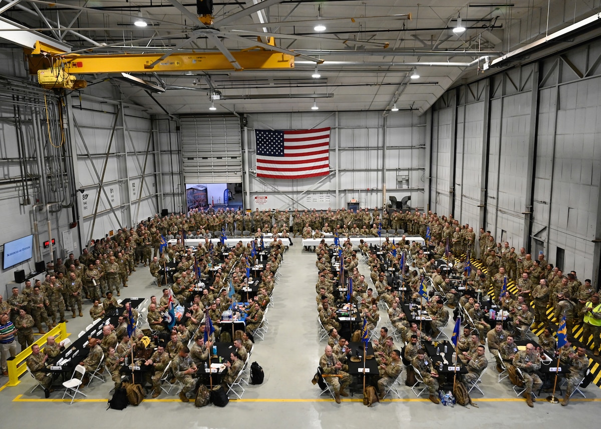 Airmen sit at tables in a hangar.