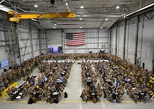 Airmen sit at tables in a hangar.