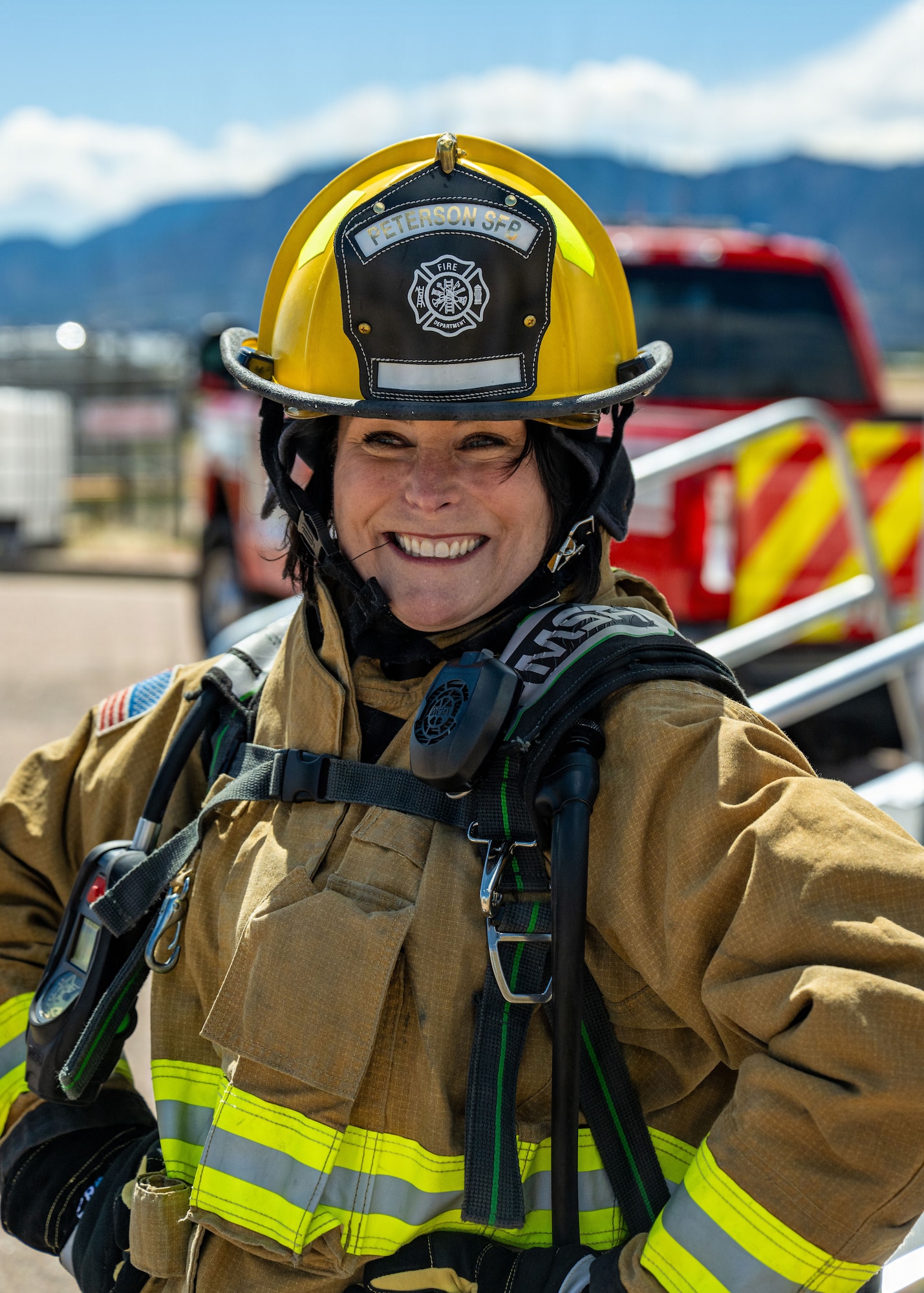 A woman smiles as she puts on fire protection gear.