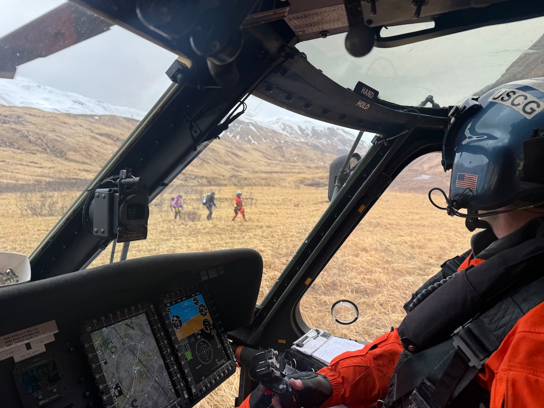 A U.S. Coast Guard pilot from Coast Guard Air Station Kodiak looks out from an MH-60 Jayhawk helicopter at two rescued hikers and a aviation survival technician in Unalaska, Alaska, March 27, 2026. The aircrew evacuated the hikers from Makushin Volcano on Unalaska Island after one of them sustained a leg injury, transporting them to emergency medical services. (U.S. Coast Guard by Lt. Cmdr. Joshua Womboldt )