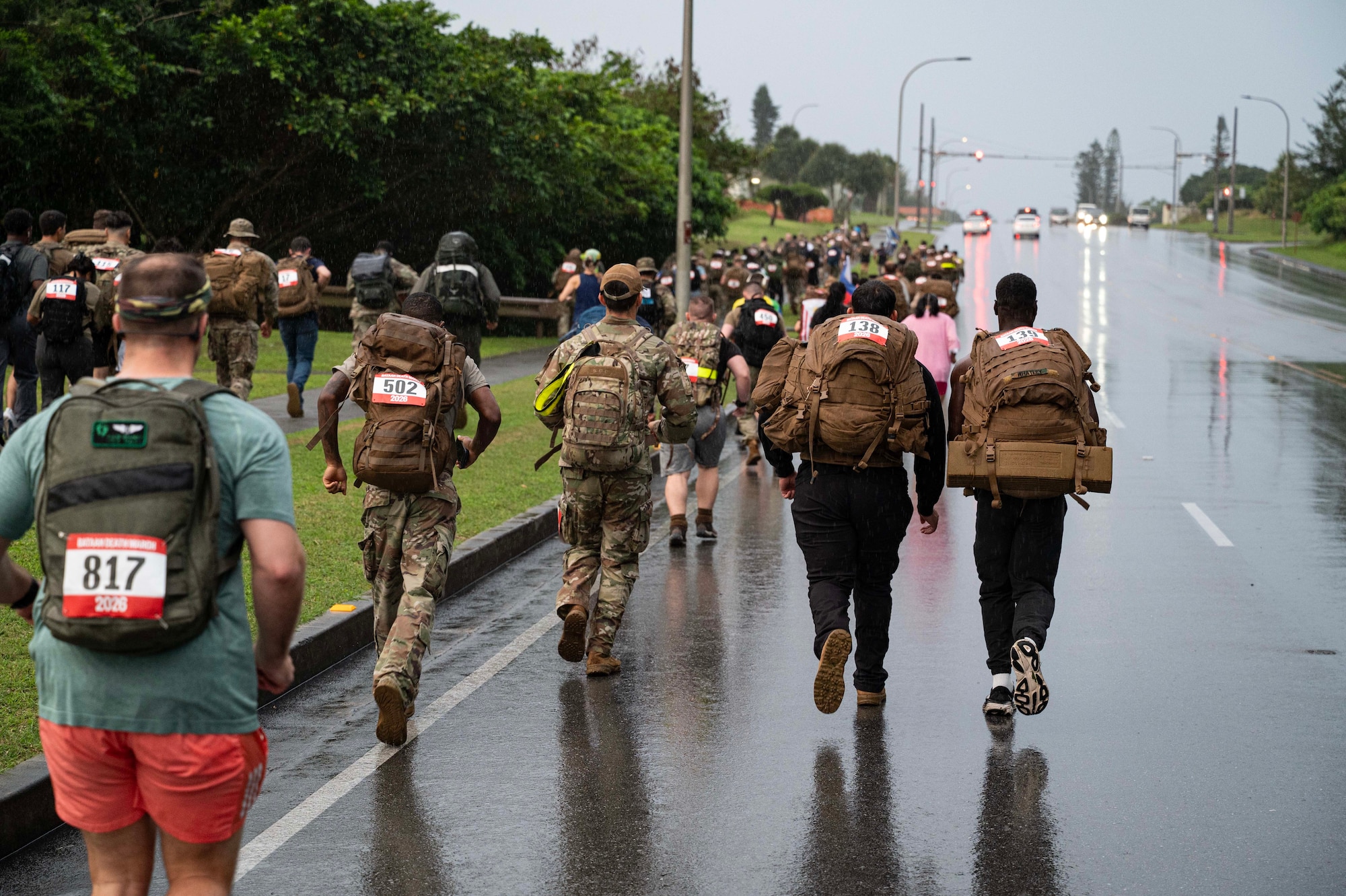 A larger group of people all walk on the road and sidewalk with bags.
