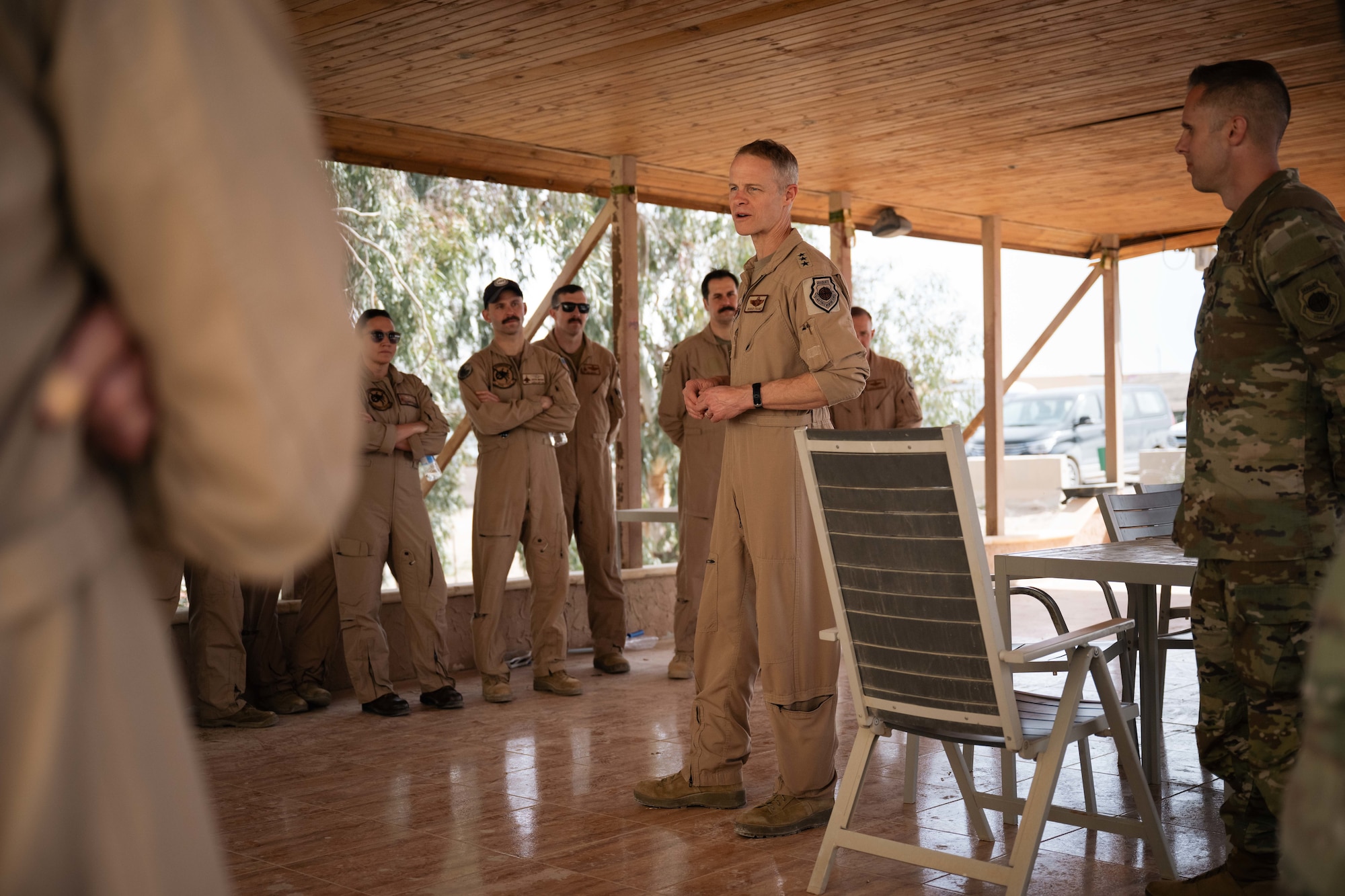 A man in a tan flight suit talks to a group of people also wearing tan flight suits.