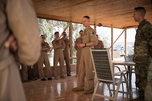 A man in a tan flight suit talks to a group of people also wearing tan flight suits.