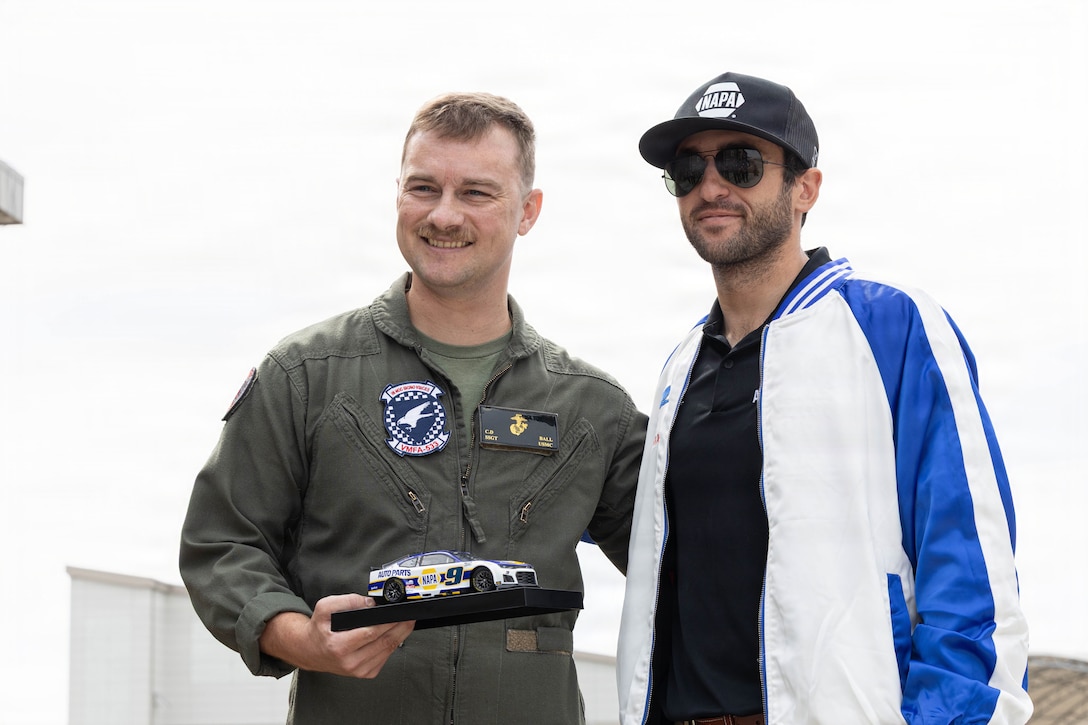 U.S. Marine Corps Staff Sgt. Collin Ball, left, from Oregon, a power line mechanic with Marine Fighter Attack Squadron (VMFA) 533, Marine Aircraft Group 31, 2nd Marine Aircraft Wing and NASCAR driver Chase Elliott pose for a photo at Marine Corps Air Station Beaufort, South Carolina, April 22, 2026. Elliott toured MAG-31 spaces to engage with Marines ahead of the Coca-Cola 600 in Charlotte, North Carolina. The Coca-Cola 600 is an annual NASCAR race held during Memorial Day weekend that historically is supported by the U.S. Marine Corps with static displays of military aircraft, vehicles and participation during the events ceremonies. (U.S. Marine Corps photo by Cpl. Mya Seymour)