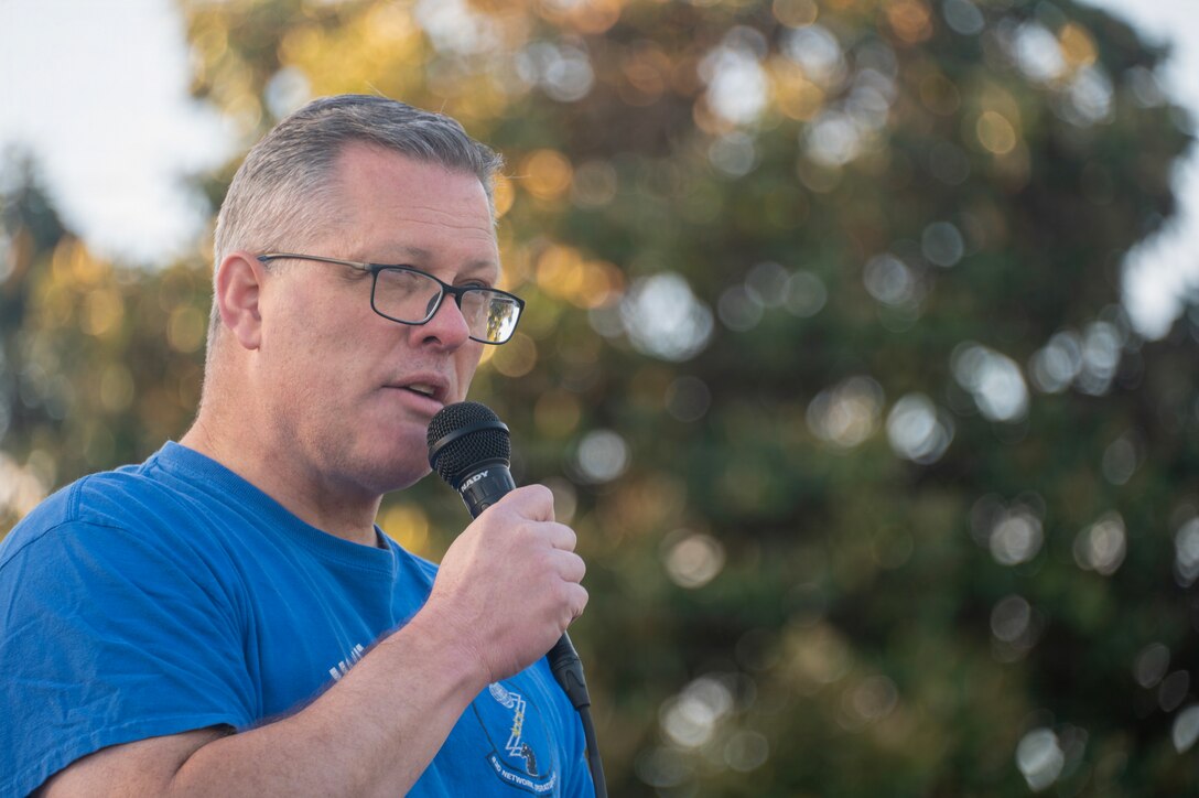 A man in a blue t-shirt is holding a microphone outdoors.