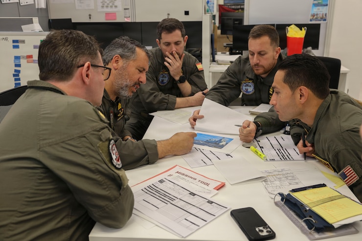 Five officials in uniform sitting around a table looking at scattered paperwork.