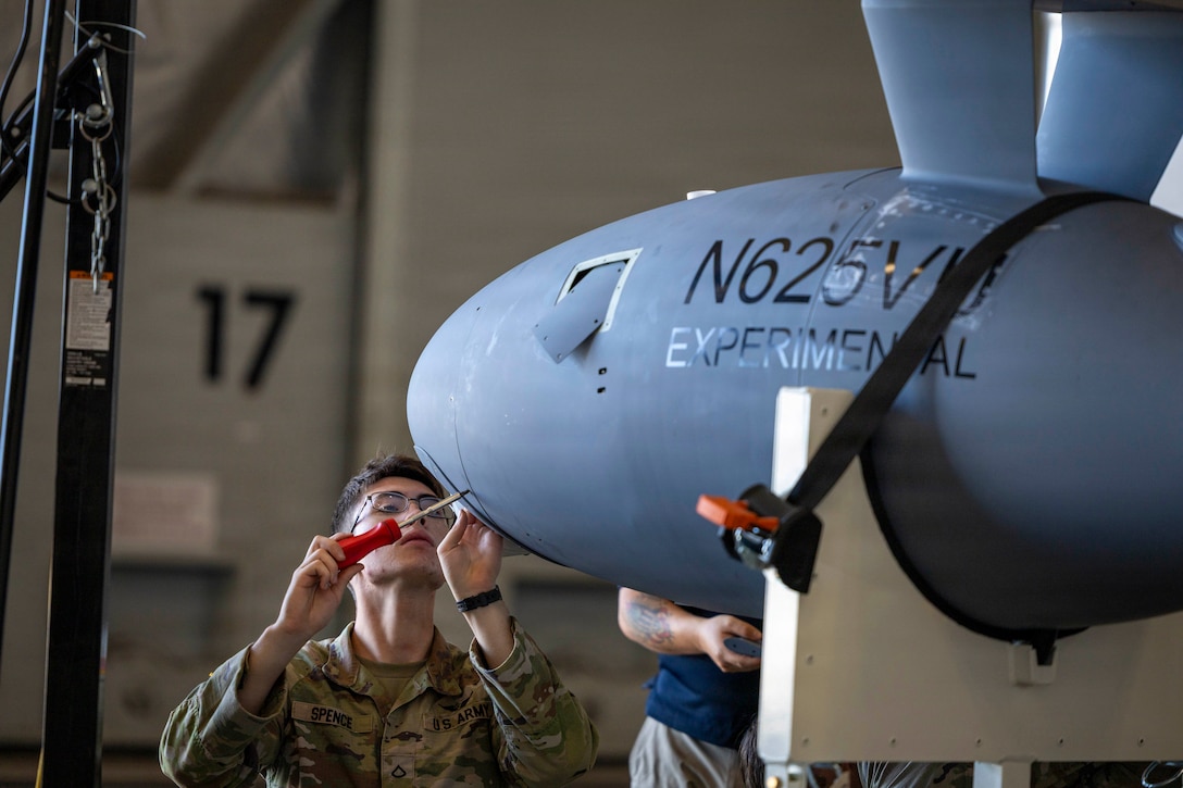 A soldier uses a screwdriver on a small aircraft.