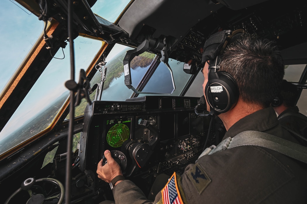A man in uniform pilots a C-130J Super Hercules aircraft.