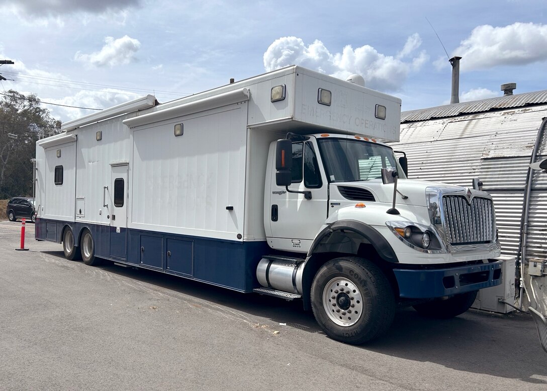A large white command vehicle sits outside.