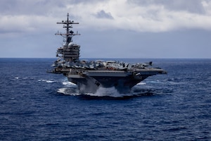 An aircraft carrier sails in the ocean, with the horizon in the background.