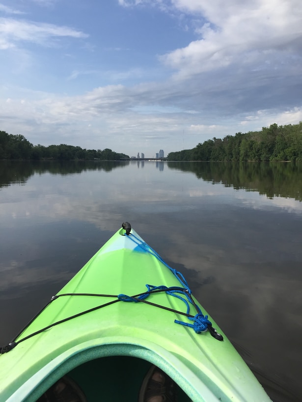 Single kayaker in green kayak paddling on calm Grand River water with wooded shoreline