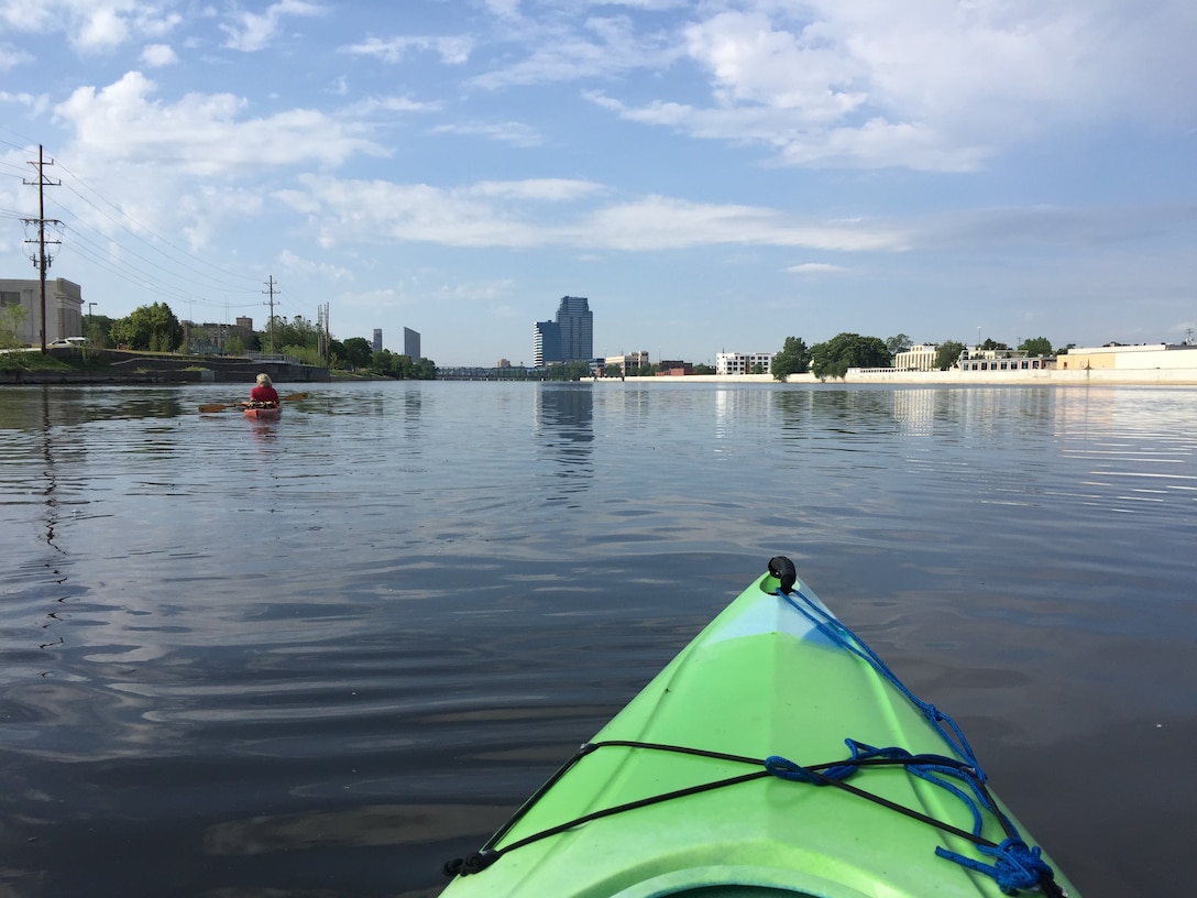 Kayaker in green kayak on Grand River with downtown buildings visible in background