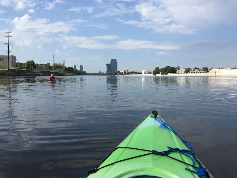 Kayaker in green kayak on Grand River with downtown buildings visible in background