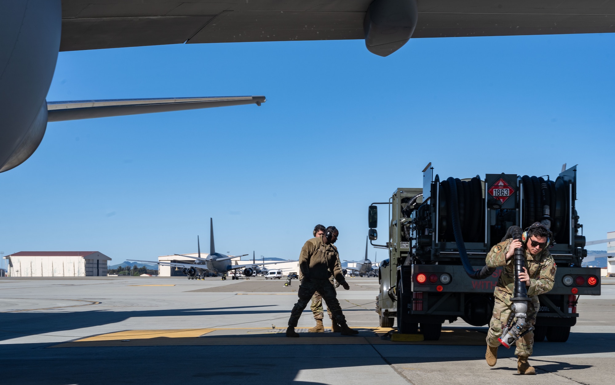 Three U.S. Airmen begin the process to fuel a KC-47 Pegasus from a fuel truck on the flight line at Travis Air Force Base.