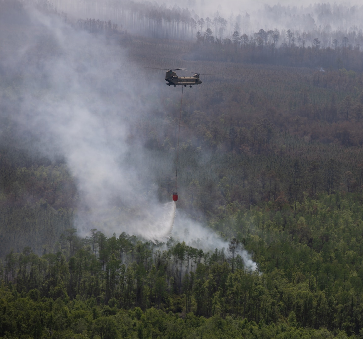 A CH-47 Chinook helicopter crew with Bravo Company, 1st General Support Aviation Battalion, 169th Aviation Regiment, 78th Aviation Troop Command, Georgia Army National Guard, dumps water with a Bambi Bucket during the wildfire suppression efforts in Pineland, Georgia, April 25, 2026. Defense plays an integral role in declared emergencies by providing a versatile and ready force capable of responding to natural and manmade disasters across the United States. (U.S. Army National Guard photo by Sgt. Jordan McNeal)