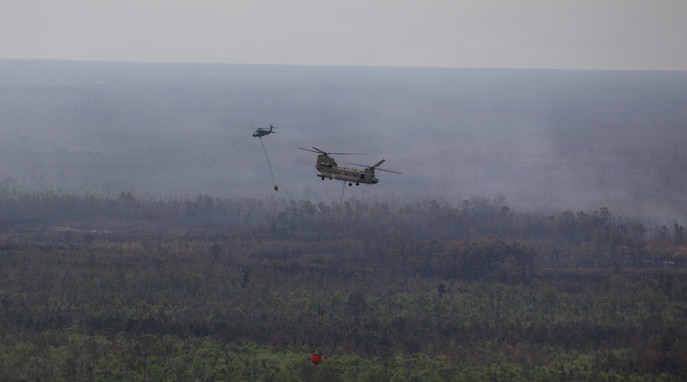 A CH-47 Chinook helicopter crew with Bravo Company, 1st General Support Aviation Battalion, 169th Aviation Regiment, 78th Aviation Troop Command, Georgia Army National Guard, and a UH-60 Blackhawk helicopter crew with Charlie Company, 1st General Support Aviation Battalion, 106th Aviation Regiment, 78th Aviation Troop Command pass each other during the wildfire suppression efforts in Pineland, Georgia, April 25, 2026. Defense plays an integral role in declared emergencies by providing a versatile and ready force capable of responding to natural and manmade disasters across the United States. (U.S. Army National Guard photo by Sgt. Jordan McNeal)