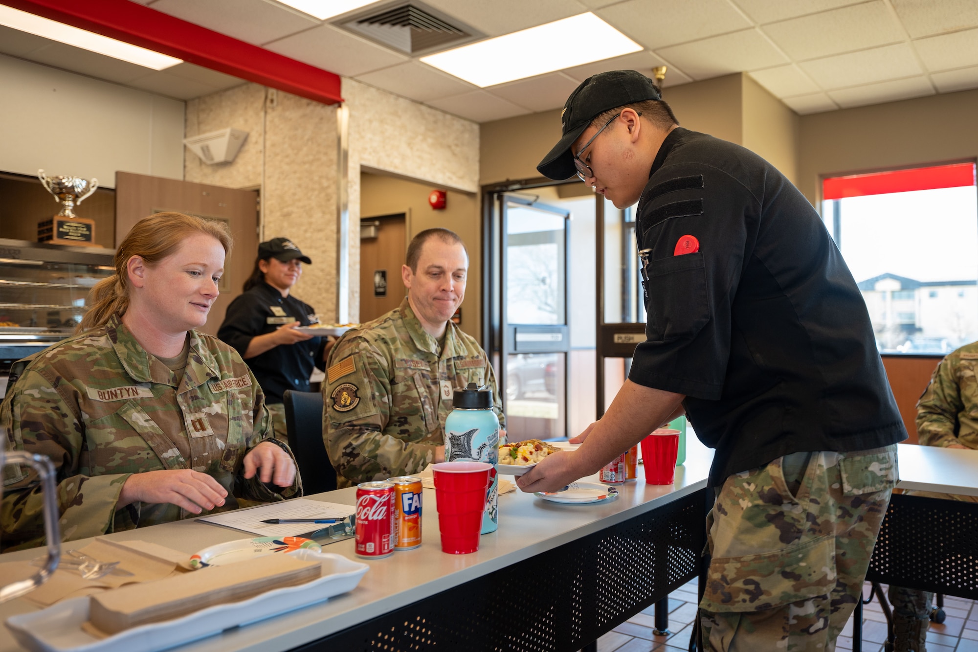 A uniformed service member serves a prepared meal to two fellow uniformed personnel.
