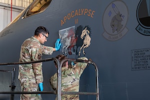 From left, U.S. Air Force Airman 1st Class Giovanni Vasquez and Senior Airman Colton Decker, both 7th Equipment Maintenance Squadron aircraft structural maintenance journeymen, apply the “Apocalypse II” nose art to a B-1B Lancer at Dyess Air Force Base, Texas, April 27, 2026. The artwork honors a fallen World War II bomber crew and completes the regeneration and visual transformation of tail number 86-0115 into the 7th Bomb Wing's flagship B-1B Lancer. (U.S. Air Force photo by Airman 1st Class William Neal)