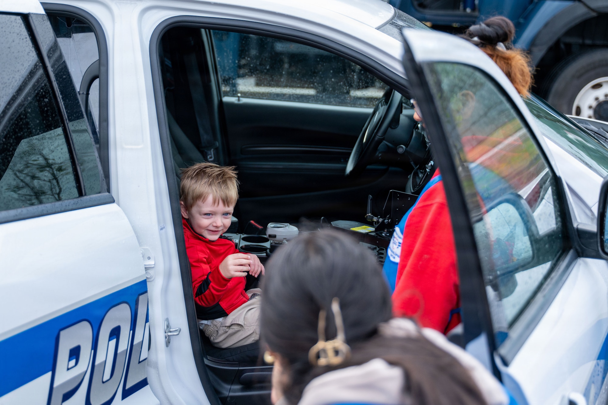 a child sits in a police patrol car and smiles for a photo