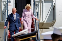 Their Majesties of the United Kingdom of Great Britain and Northern Ireland, King Charles III and Queen Camilla, descend the stairs of a United Kingdom aircraft during a military arrival ceremony.