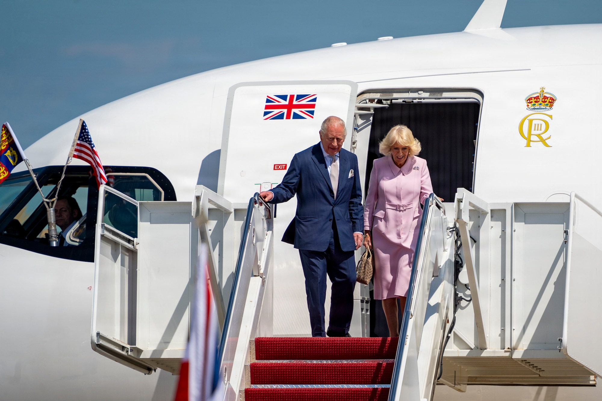 Their Majesties of the United Kingdom of Great Britain and Northern Ireland, King Charles III and Queen Camilla, descend the stairs of a United Kingdom aircraft.