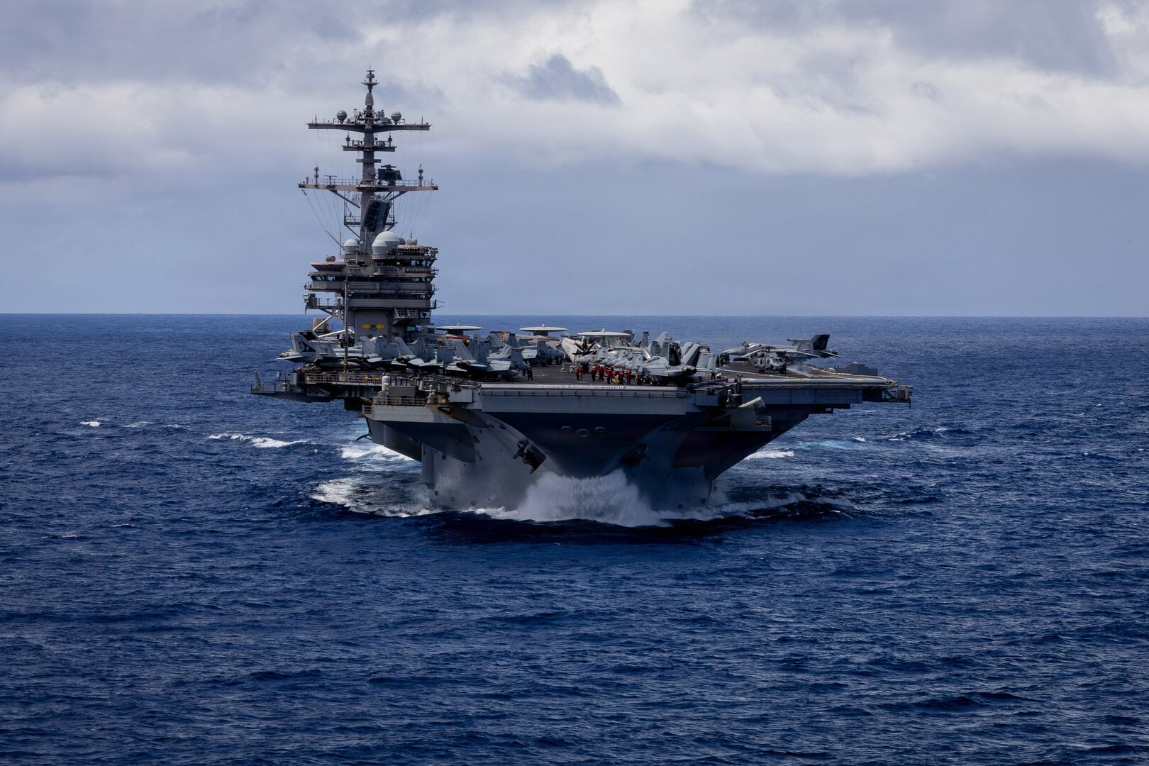 An aircraft carrier sails in the ocean, with the horizon in the background.