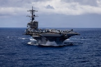 An aircraft carrier sails in the ocean, with the horizon in the background.