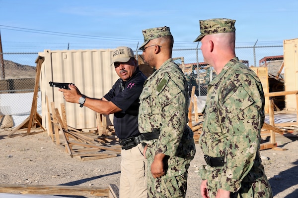 Provost Marshal’s Office Training Sgt. Juan Montero (left) instructs Hospital Corpsman 2nd Class Aijalon Newbern (center) and Cmdr. William “Bill” Lawson, both assigned to Navy Medicine Readiness and Training Command Twentynine Palms, on proper firing and reloading techniques with the M9 service pistol during training at Marine Corps Air Ground Combat Center Twentynine Palms, Calif., March 26, 2026. (U.S. Navy photo by Christopher Jones, NMRTC/NH Twentynine Palms public affairs officer)