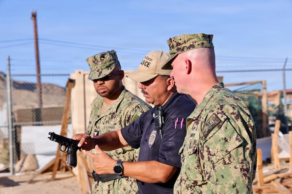 Provost Marshal’s Office Training Sgt. Juan Montero (center) instructs Hospital Corpsman 2nd Class Aijalon Newbern (left) and Cmdr. William “Bill” Lawson, both assigned to Navy Medicine Readiness and Training Command Twentynine Palms, on proper firing and reloading techniques with the M9 service pistol during training at Marine Corps Air Ground Combat Center Twentynine Palms, Calif., March 26, 2026. (U.S. Navy photo by Christopher Jones, NMRTC/NH Twentynine Palms public affairs officer)