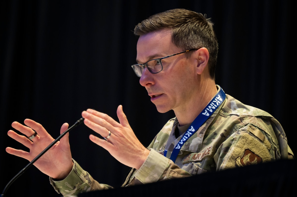 Man in Air Force camo talks while using his hands. He is seated.