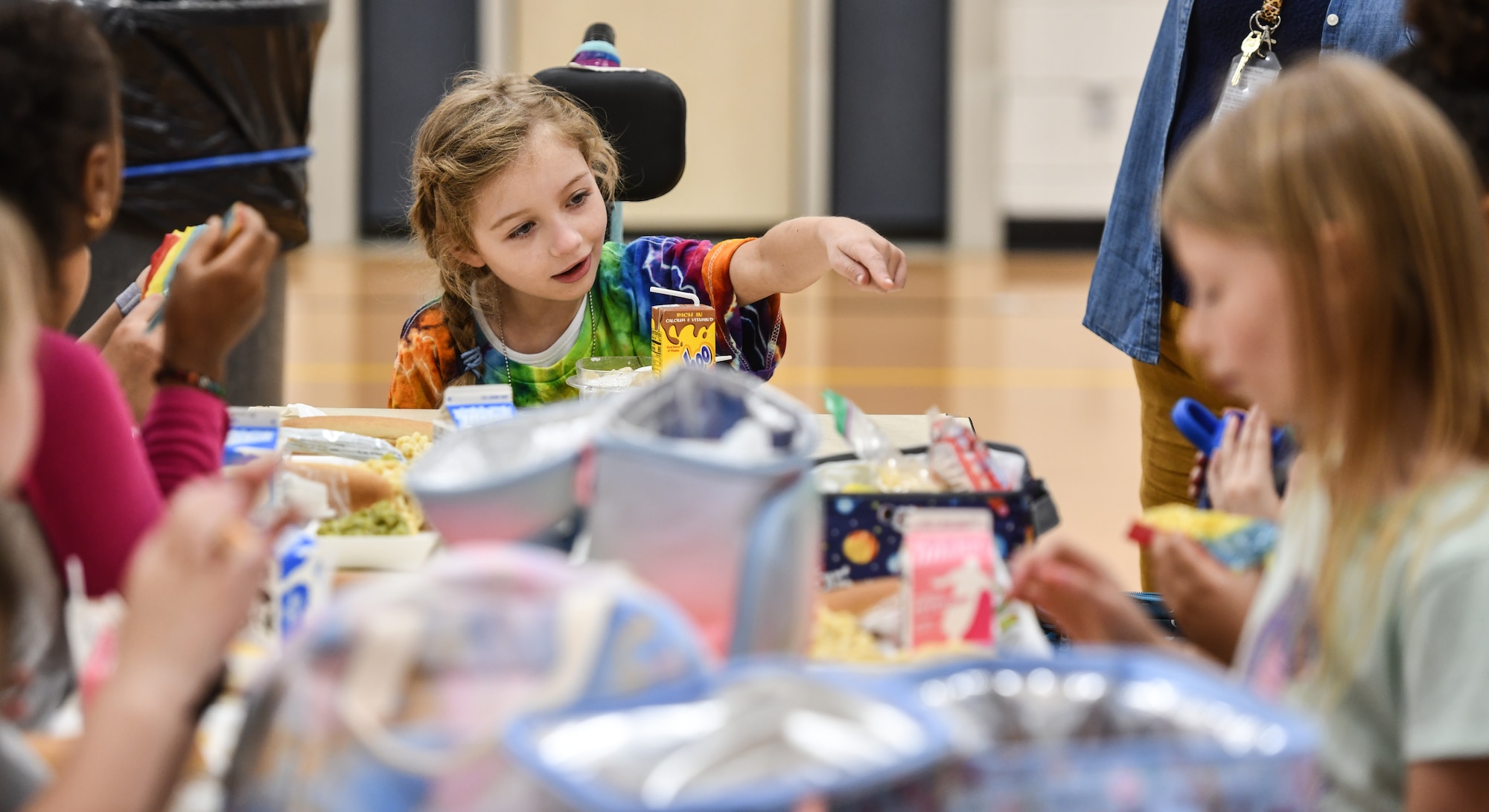 Hannah interacts with her classmates during lunchtime at Leonard Lawrence Elementary school in Bellevue, Neb. on April 22, 2026. Where she once was in a fully special needs classroom, she is now integrated into a normal second grade class, and is on par academically with her age group. (U.S. Air Force photo by Chad Watkins)