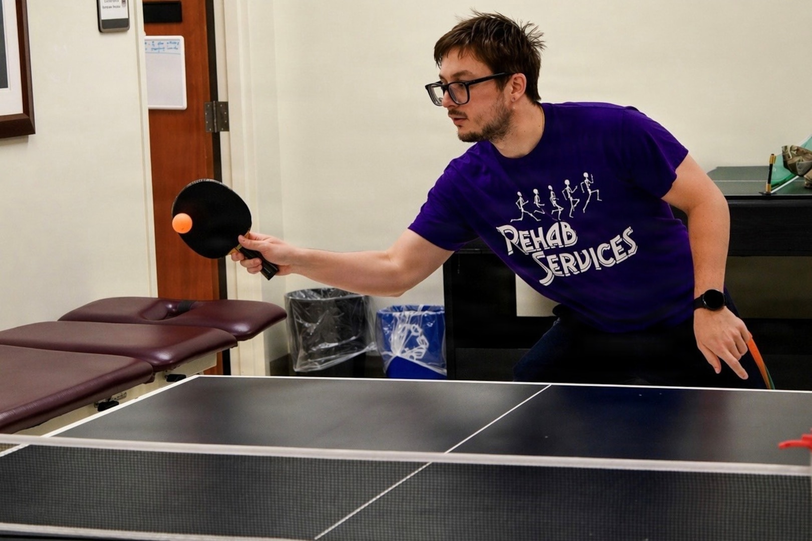 Man in purple shirt plays ping pong.