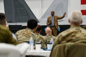 Dixon stands holding a microphone in front of an audience of Airmen.