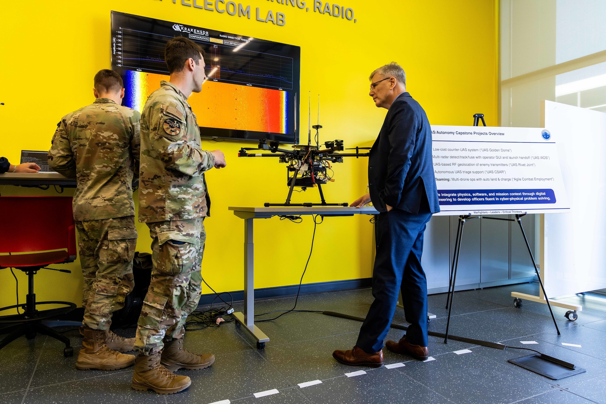 Two Airmen in uniform show a drone on a table to the Secretary of the Air Force.