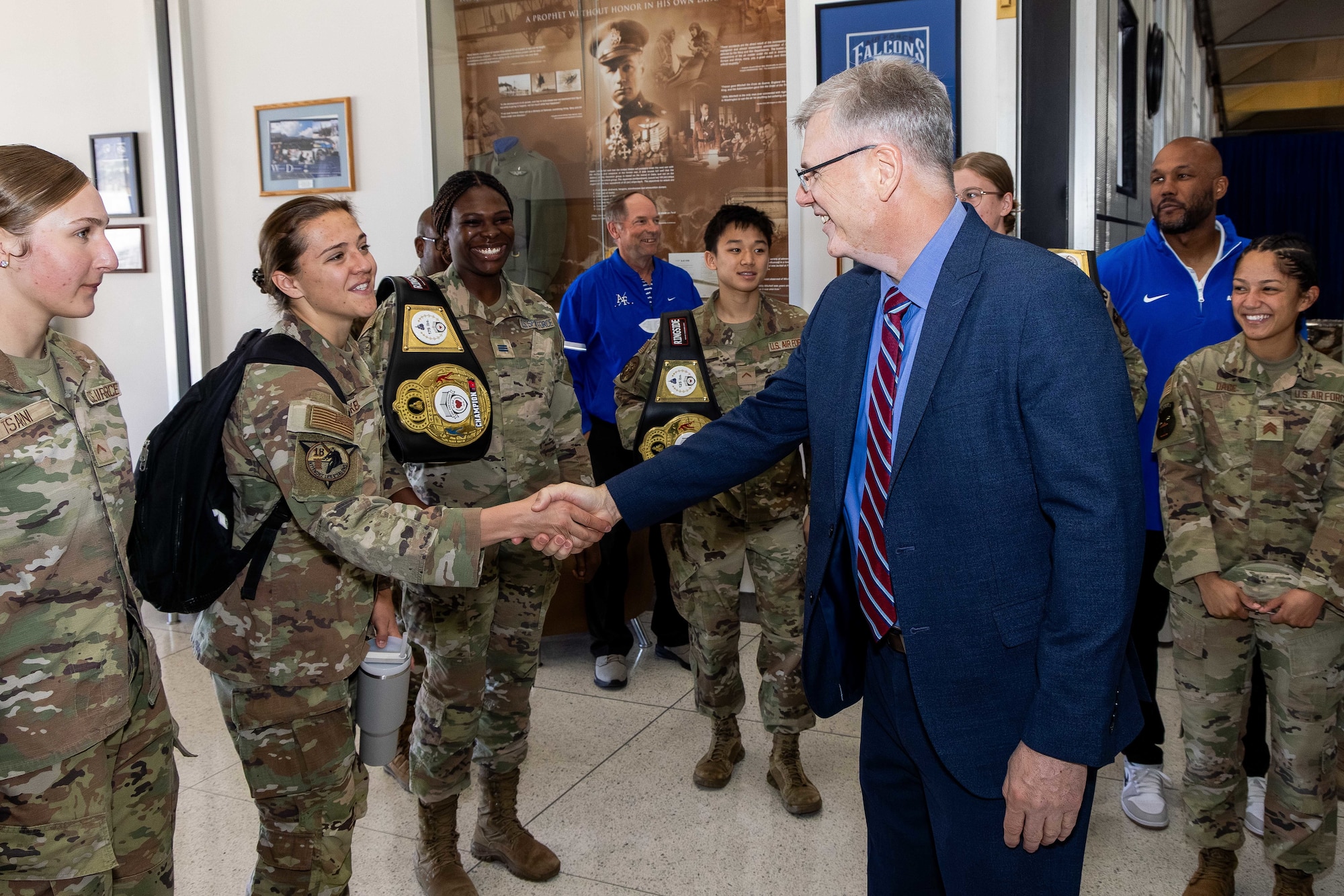 A man in a suit shakes hands with a cadet in front of her peers.