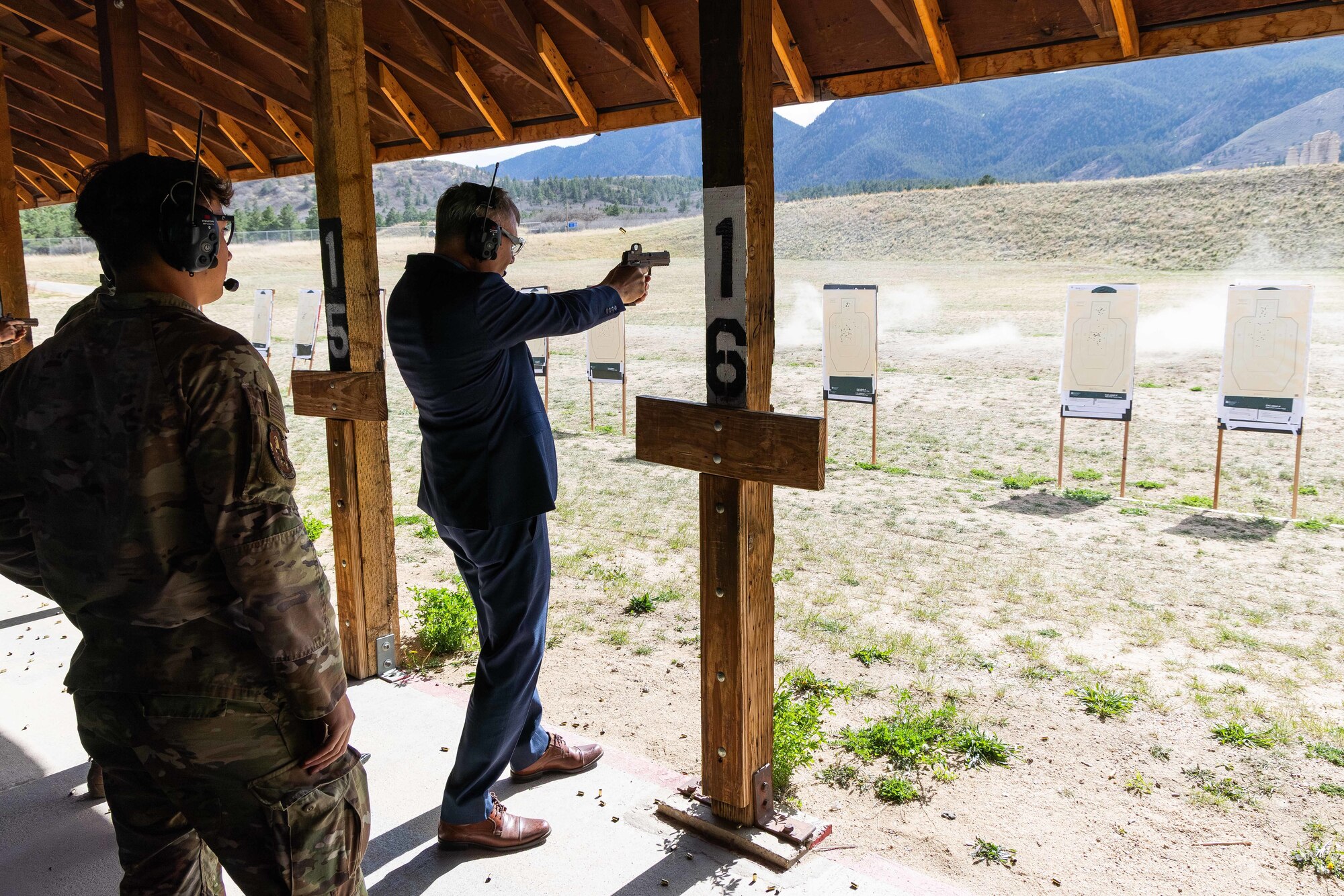 A firing range instructor observes the Secretary of the Air Force shooting at targets.