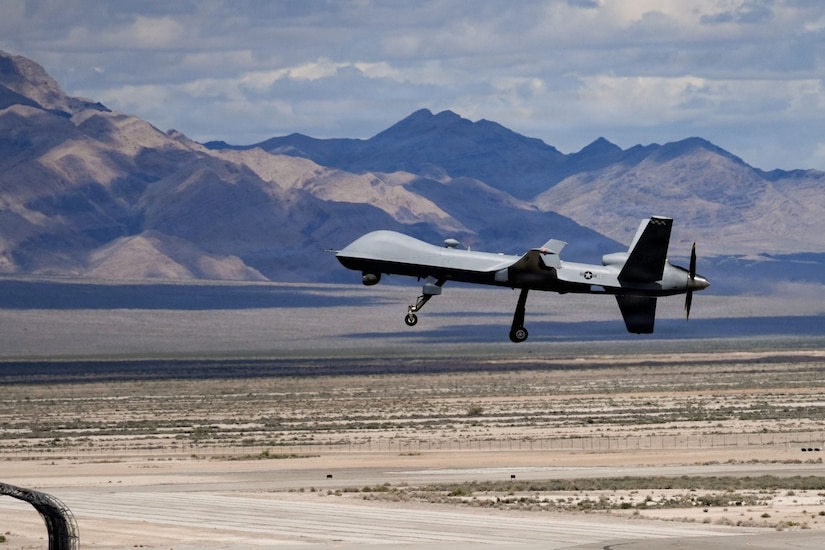 An unmanned aircraft takes off from a flight line in desert-type terrain with mountains in the background.